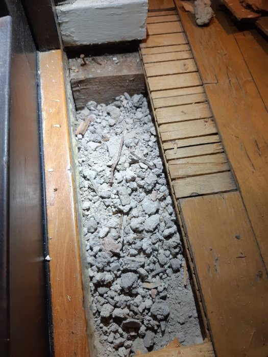 Ett hål i ett gammalt parkettgolv visar träreglar och murbruk, vilket indikerar golvets konstruktionsmetod från förr.