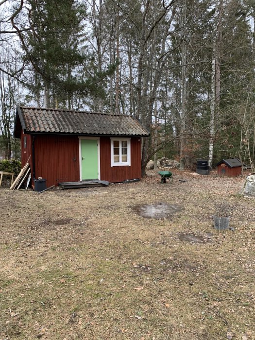 Röd trästuga med gröna detaljer i skogsmiljö, ska renoveras med nytt badrum.