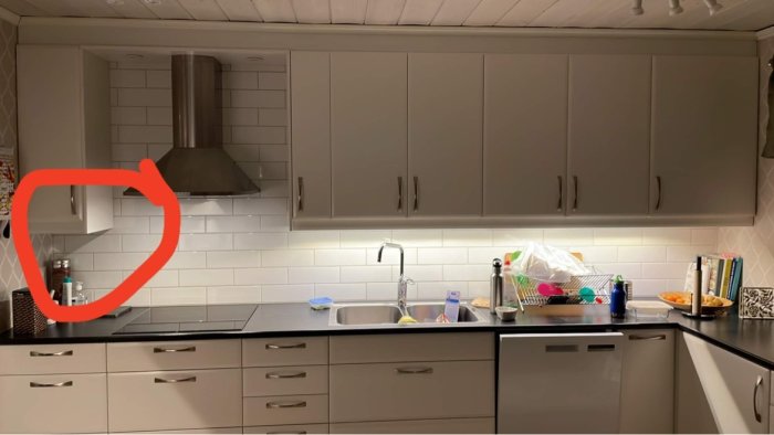 Kök med bänkar och skåp under belysning, diskho, och köksutrustning på bänken.