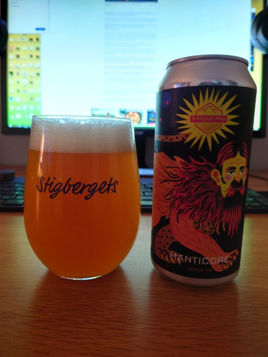 Ett ölglas fyllt med öl framför en dator, bredvid en burk av Manticore Triple IPA från Basqueland Brewing.