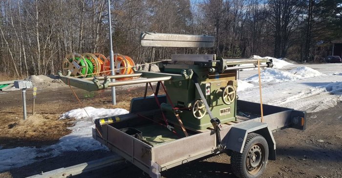 En träbearbetningsmaskin fastsäkrad på en släpvagn parkerad utomhus med snö i bakgrunden.