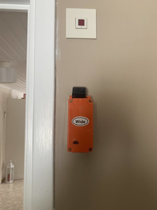 Orange Frico-enhet märkt med "Wide" monterad på en vägg under en strömbrytare.