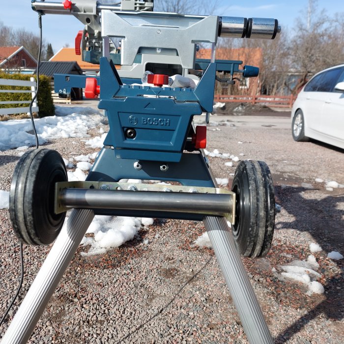 Egenbyggd konstruktion av en Bosch-bordsåg monterad på en vagn med hjul utomhus med snöfläckar och en vit bil i bakgrunden.