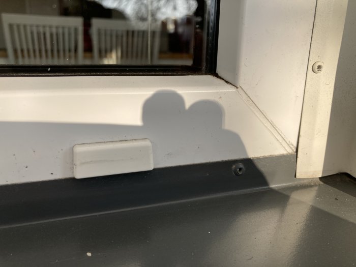 Skugga av ett fönsterlås på en fönsterbräda vid ett smutsigt fönster i solljus.