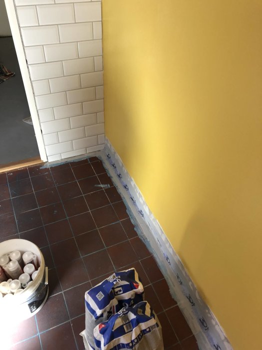 Renoverad tvättstuga med nymålade gula väggar, vita kakelplattor och målarutrustning på golvet.