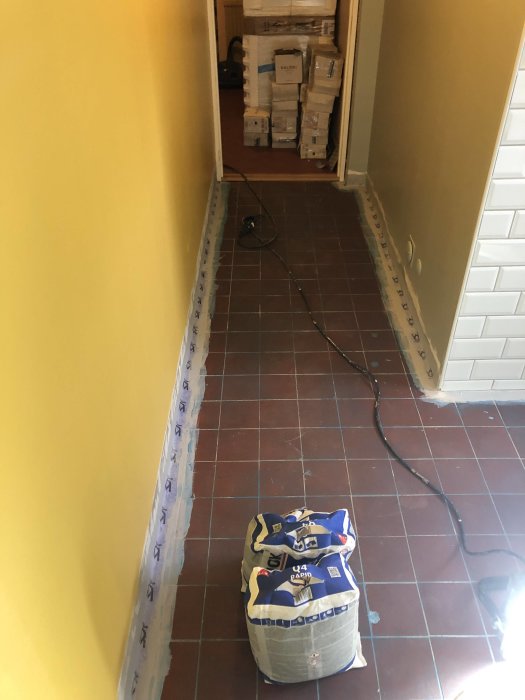 Renoveringsarbete i en korridor med gula väggar och en säck byggmaterial på golvet.