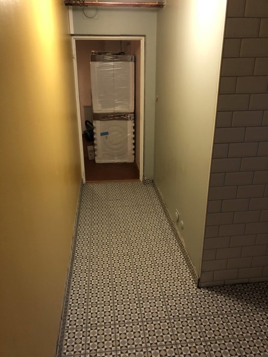 Renoverad korridor med mönstrade klinkergolv som leder till tvättstugan med synliga vitvaror.