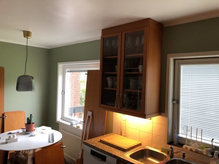 Uppfräschade köksinteriör med träskåp och grön vägg, inklusive ett fönster med persienner.