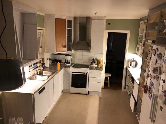 Ett kök under renovering med vit skåpinredning, en del luckor borttagna eller öppna och köksredskap synliga.