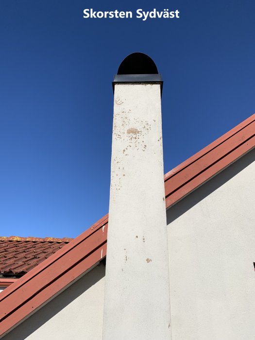 Skorsten med rostfläckar på ett hus under en klarblå himmel.