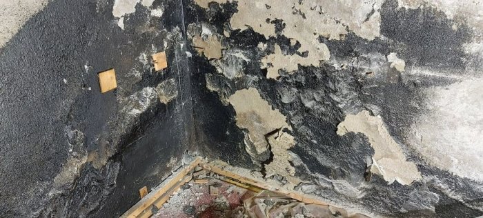 En vägg med potentiellt svartmögel och lager av puts som faller av, träreglar och spillror på golvet.