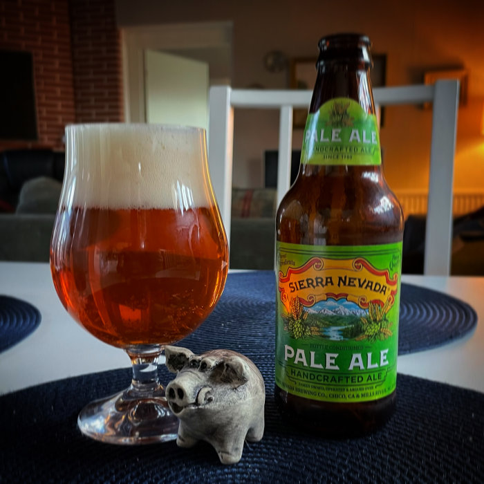 Ölglas fyllt med bärnstensfärgad dryck bredvid Sierra Nevada Pale Ale-flaska och en prydnadsgris.
