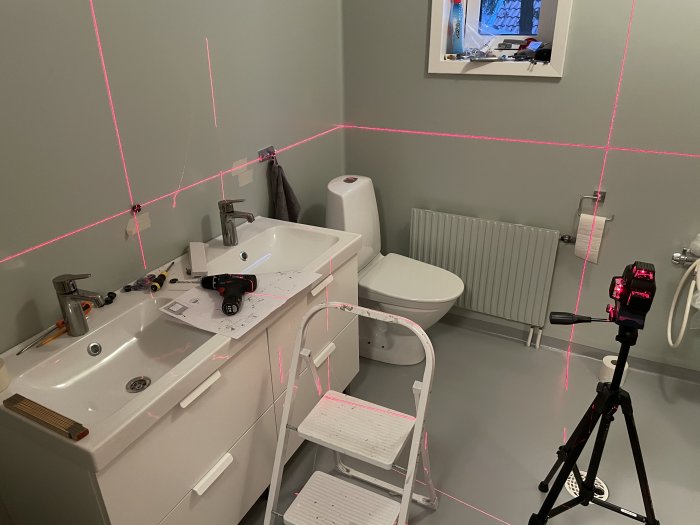 Badrum med laserinstrument som projicerar röda linjer för montering av spegel.