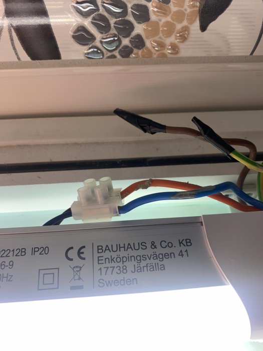 Elanslutningar med tejpade ledningar framför lampa, detalj av etikett från BAUHAUS.