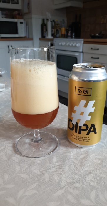 Ölglas med överskummat öl bredvid en burk Double IPA på ett köksbord.