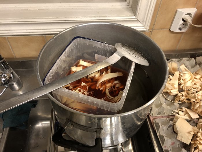Tändkrusiduller av träspån doppar i smält stearin i en kastrull på ett köksbänk.