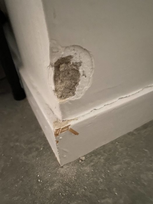 Spricka och skada på en vitmålad vägghörn orsakad av en dammsugare.