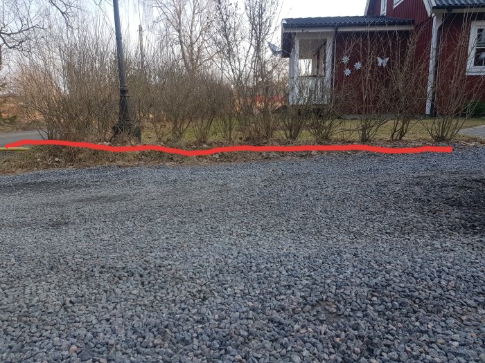 Grusplan med en röd linje som markerar den tänkta murens plats framför en häck och rött hus.