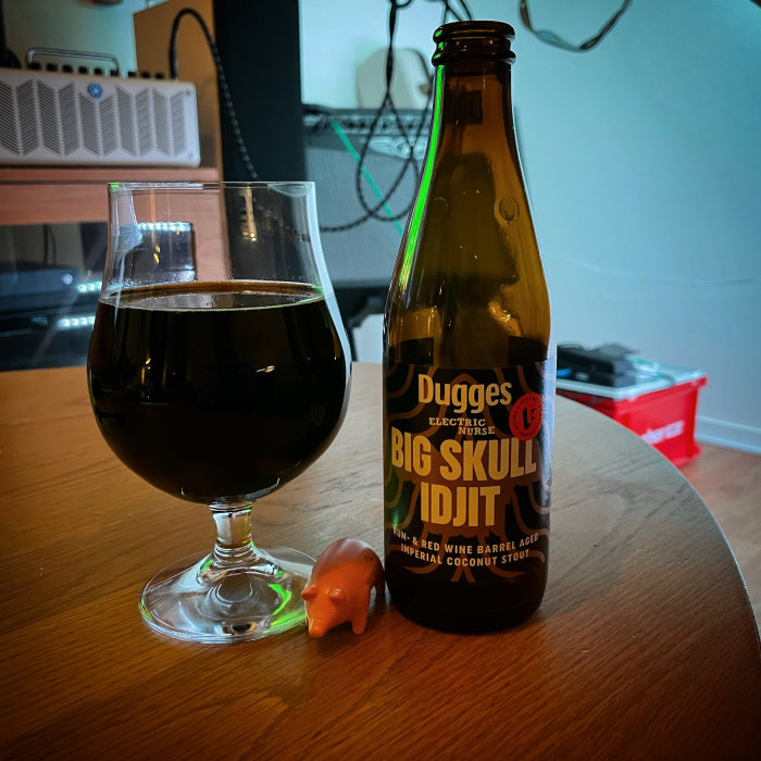 Mörkt öl i ett glas bredvid en ölflaska och en liten plastfigur av ett djur på ett bord.