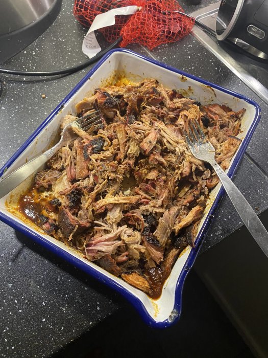 Grillad pulled pork i ugnsform med gafflar som river köttet.