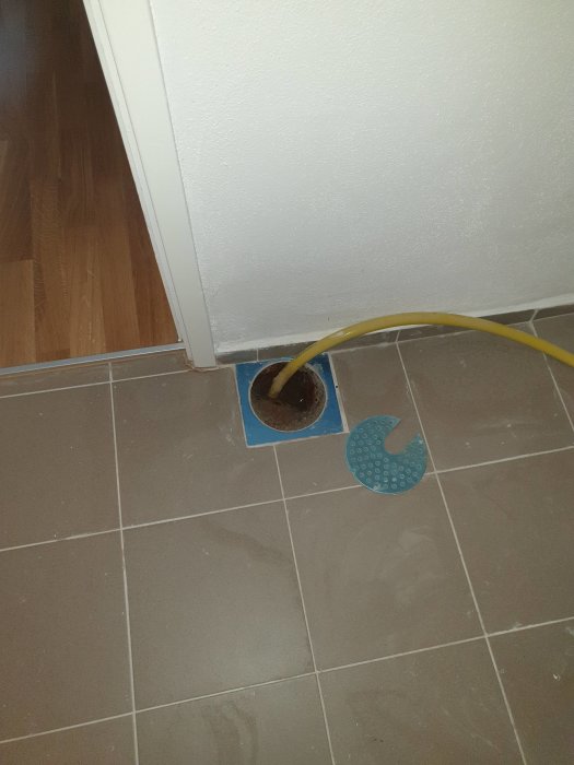 Brunn utan klämring i kaklat golv bredvid en dörr, felaktigheter som kan leda till vattenskador.