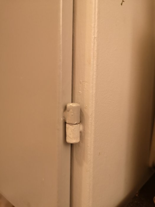 Dörr med övermålat gångjärn som visar spår av slarvig målning.