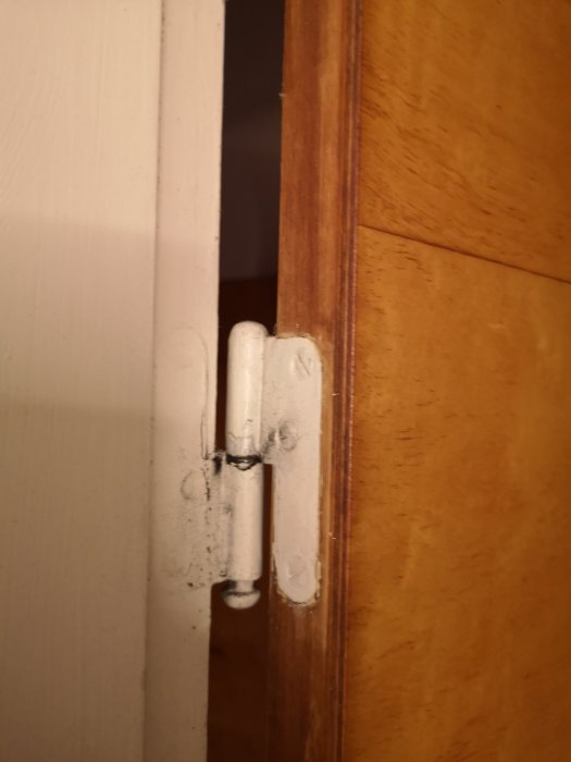 Dörrgångjärn med övermålade skruvhuvuden och färgstänk på karmen.