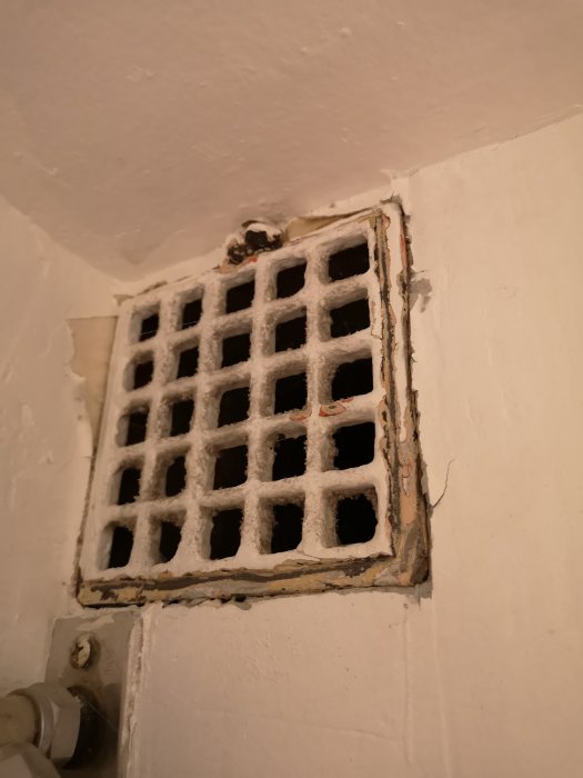 Ventilationsgaller i vägg med slarvig målarfärg över skruvar och kanter.