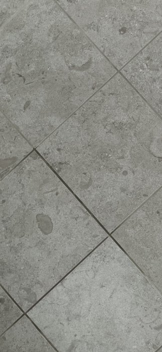 Golvplattor med ojämnt färgade fogar, vissa partier mörkare än andra.