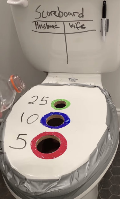 Toalettsits med hål utsedda med poäng, på cisternen en poängtavla skrivet "Husband" och "Wife".