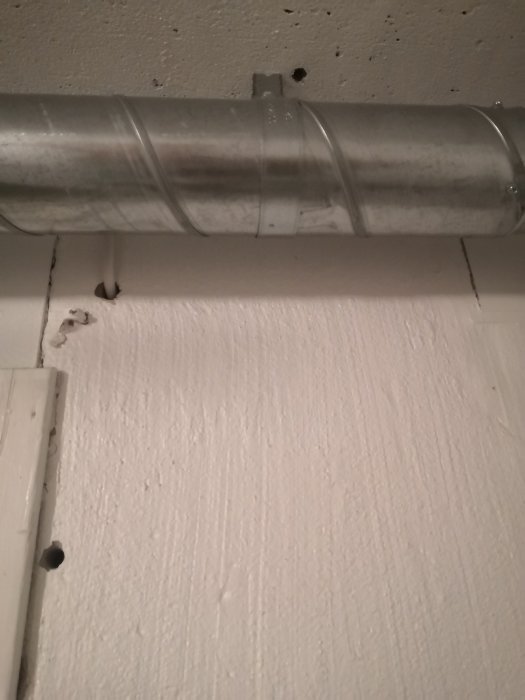 Ventilationsrör längs taket och putsad betongvägg där putsen släppt på en källarhall.