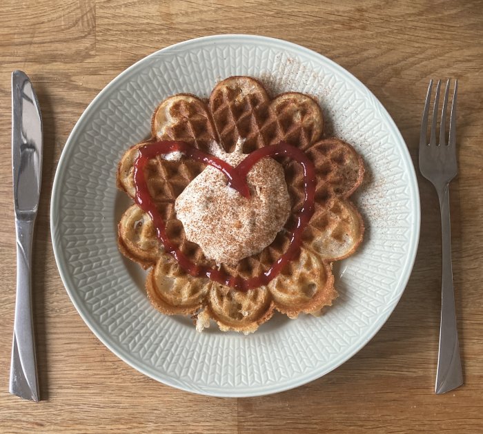 Våfflor med sylt och pudrat socker på tallrik med bestick på träbord.