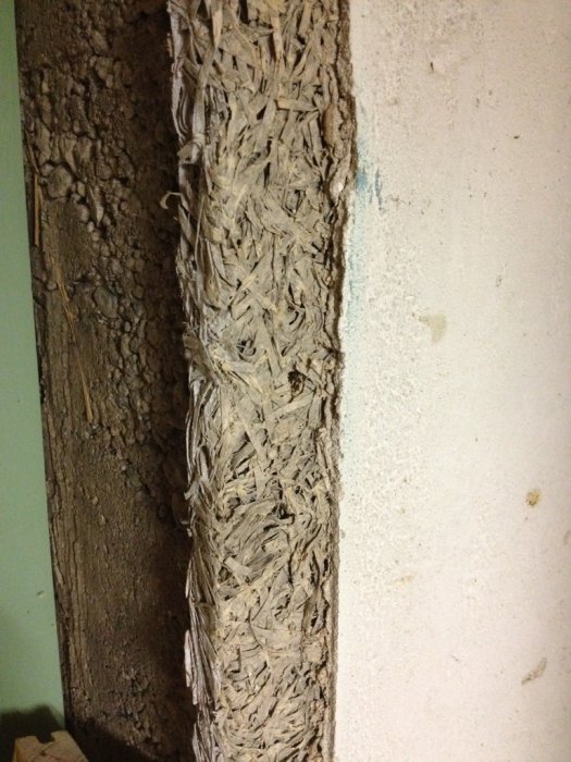 Vægbillede af mineraluld eller fibermateriale, der er monteret i en kælder. Overfladen ser grov og vanskelig at fastgøre ting i.