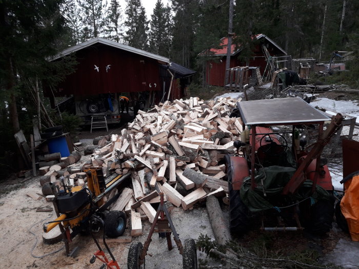 Hemmagjord vedklyv av skrot framför en hög med klyvd ved och verktyg utspridda.