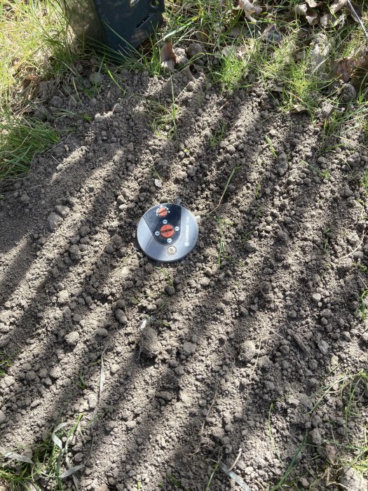 Popupsprinkler delvis nedgrävd i jord med gräs runtomkring.