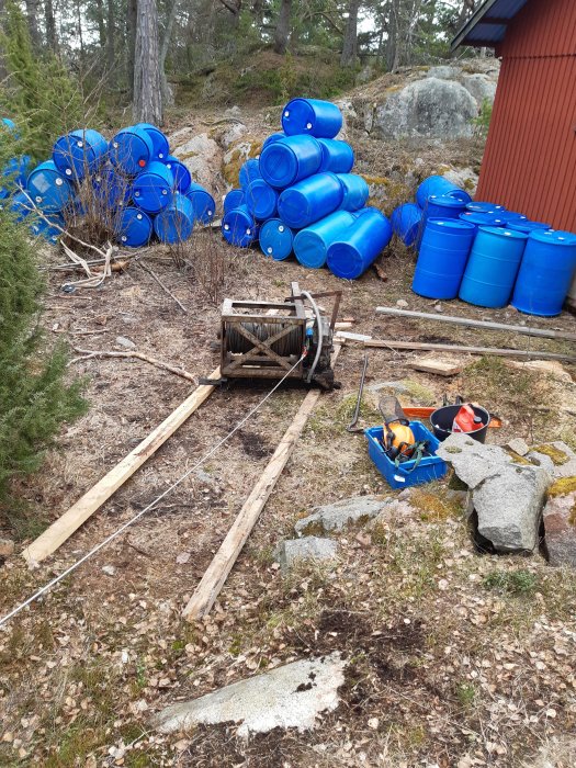 Nyinstallerad vinsch bredvid gamla järnvägsräls i skog med blåa tunnor och verktyg i bakgrunden.