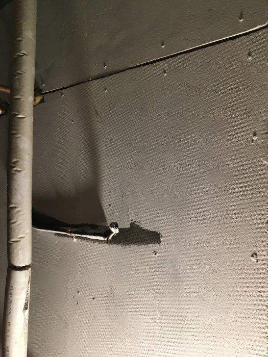 Strukturerat takmaterial med vit färg, grått omålat område under kabel, möjlig asbest.