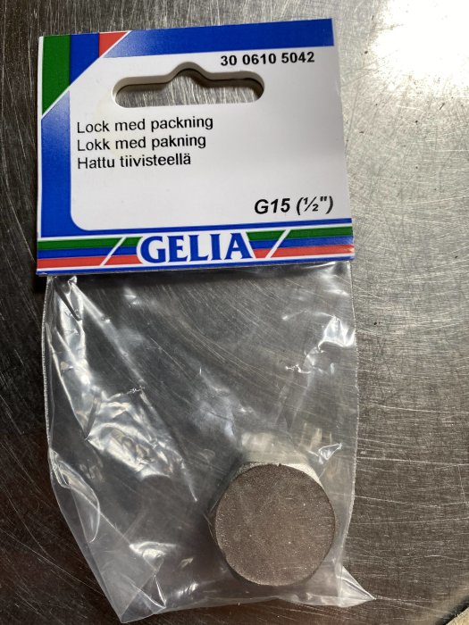 Lock med packning från Gelia för rör G15 (1/2 tum) ligger förpackat på ett metallbord.