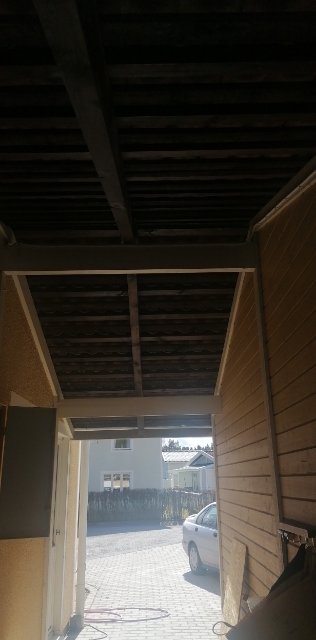 Utsikt från en oisolerad takstomme med synliga reglar och undersidan av takpannor, i en blivande hall.