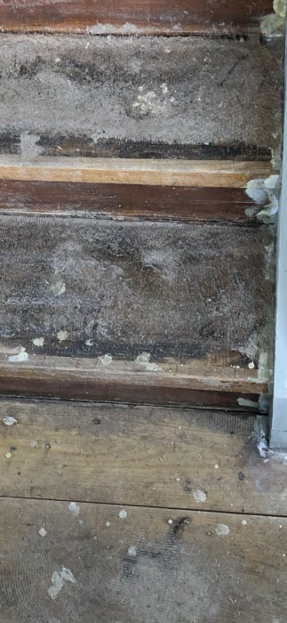 Delvis bortriven äldre plastmatta på en trätrappa, synliga spår av lim och möjlig nedsmutsning.