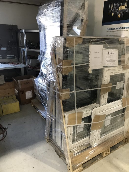 Staplad och plastfolieinslagen fönsterbeställning på en pall i ett lagerutrymme.