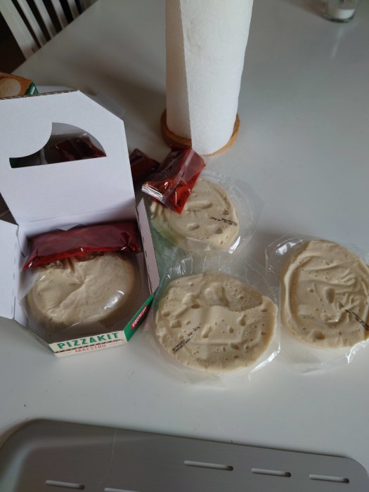 Förpackade pizzadegar från Pop! Bakery lättutbakade, på ett köksbord med en öppen degbox.