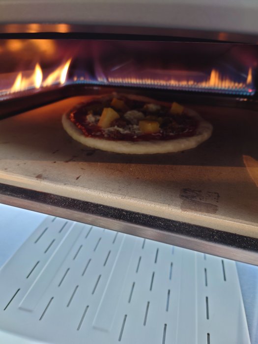 Hembakad pizza med ananas och köttfärs på stenplatta i ugn, bakad på Pop! Bakerys deg.