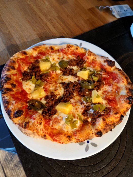 Hembakt pizza med tomatsås, ost, ananas, jalapeños och köttfärs på vit tallrik.