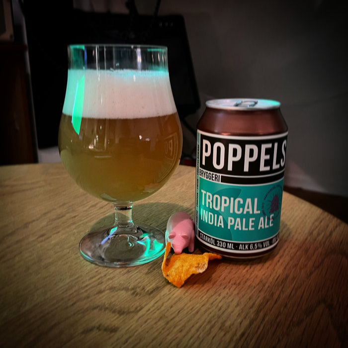 Ett glas med öl och en Poppels Tropical India Pale Ale burk med en chipsbit och en liten figur.