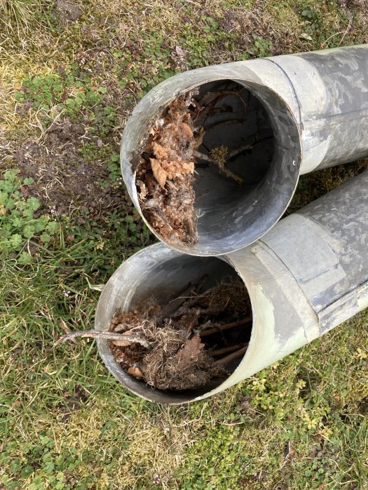 Ventilationsrör med igentäppt ände fyllt med skräp och organiskt material på marken.