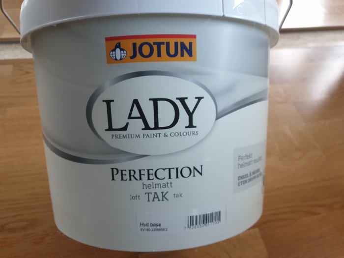 En burk med Jotun Lady Perfection takfärg i vit bas på ett trägolv, med texten "Perfekt helmatt resultat" visible.