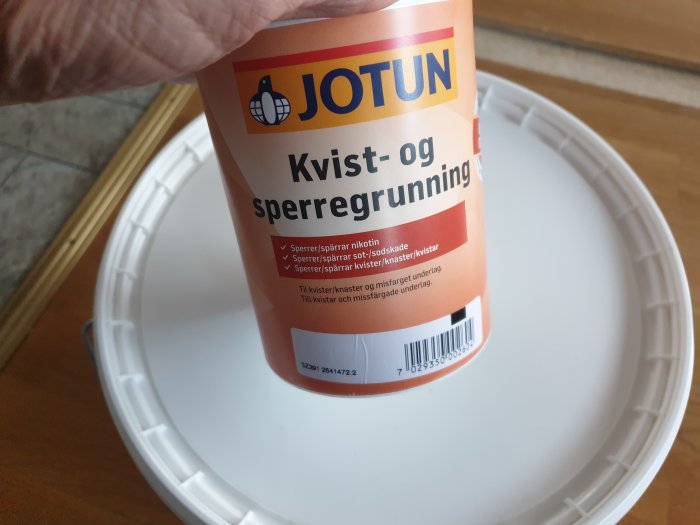 Hand håller en burk Jotun kvist- och spärrgrundfärg nära en vit målburk.