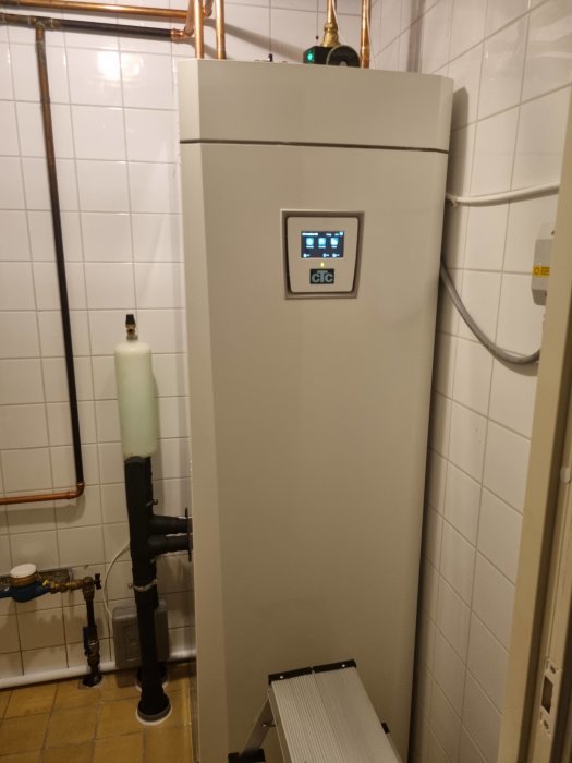 Nytt installerat värmepumpssystem med digital display i ett pannrum, kopplat till rör och shuntar.