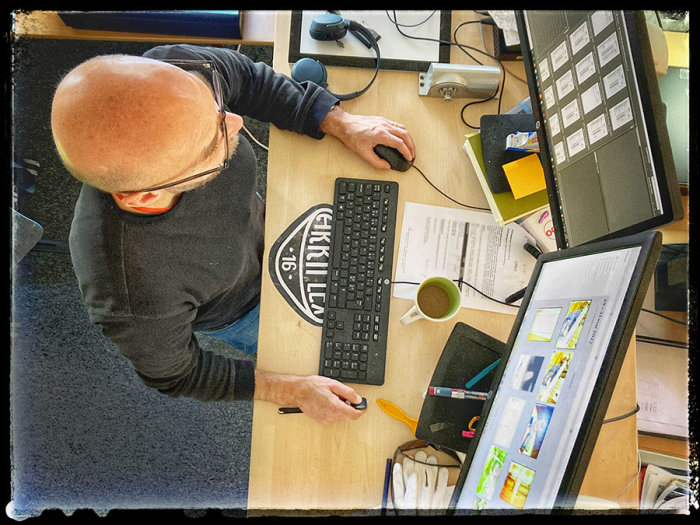 Person som arbetar vid en skrivbord med två datorskärmar och tangentbord, omgiven av anteckningsblock och en kaffekopp.